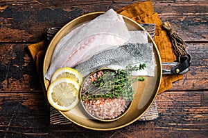 Uncooked Raw Sea Bass fillets, Seabass fish with thyme, pink salt and lemon. Dark background. Top view