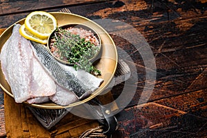 Uncooked Raw Sea Bass fillets, Seabass fish with thyme, pink salt and lemon. Dark background. Top view. Copy space