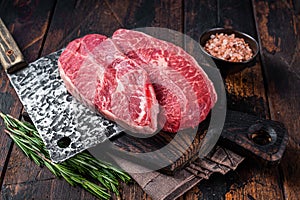 Uncooked Raw Shoulder Top Blade or flat iron beef meat steaks on a wooden butcher board with meat cleaver. Dark wooden