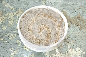 Uncooked rice in white ceramic bowl on metal background