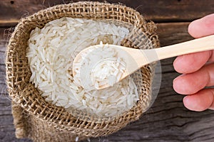 Uncooked rice in a wooden spoon over small burlap sack.