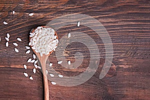 Uncooked rice in the wooden spoon top view.