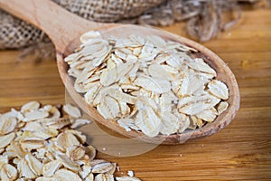 Uncooked rolled oats in wooden spoon and beside, close-up
