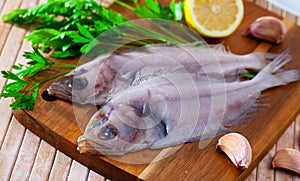 Uncooked roosterfish with greens and garlic on wooden board