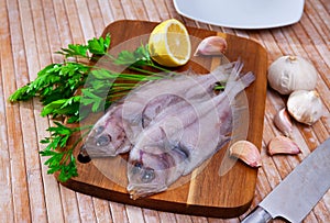 Uncooked roosterfish with greens and garlic on wooden board