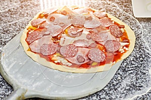 Uncooked salami pizza on pizza peel.