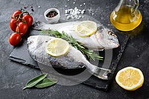 Uncooked sea bream fish, olive oil, lemon and spices on slate