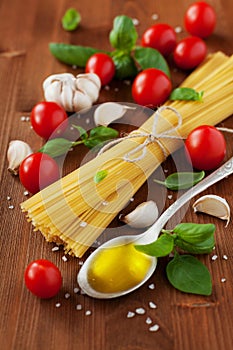 Uncooked spaghetti, cherry tomato, basil, garlic and olive oil, ingredients for cooking pasta, food background