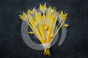 Uncooked Spaghetti Penne Pasta Arranged in Composition of Wheat Ears Bouquet on Black Stone Background. Menu Poster Template