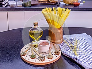 Uncooked spaghetti in wooden pot and spices on wooden plate