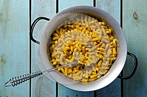 Uncooked spiral pasta with a spoon in a strainer.