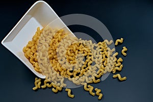 Uncooked spiral pasta sprinkled from a white plate on a dark table