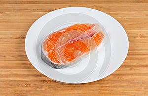Uncooked steak of arctic char on dish on wooden surface