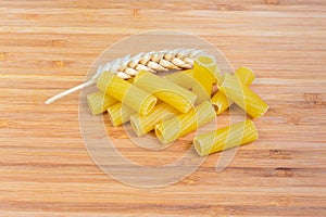 Uncooked tortiglioni pasta and wheat ears closeup on wooden surface