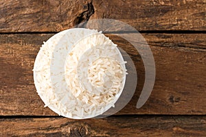 Uncooked white rice in bowl on rustic wooden table.