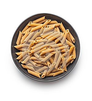 Uncooked whole grain pasta isolated on white background. Raw penne pasta on plate