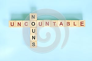 Uncountable nouns concept in English grammar noun education. Wooden block crossword puzzle flat lay in blue background.