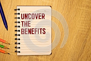 Uncover the Benefits - text written on notebook on wooden table with pen coffee and glasses
