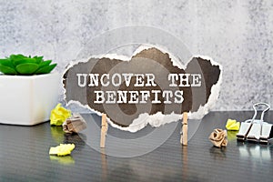 Uncover the Benefits - text written on notebook on wooden table with pen coffee and glasses