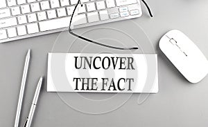 UNCOVER THE FACT text on paper with keyboard on grey background