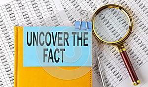 UNCOVER THE FACT text on sticker on notebook with magnifier and chart. Business