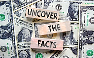 Uncover the facts symbol. Concept words Uncover the facts on wooden blocks on a beautiful background from dollar bills. Business