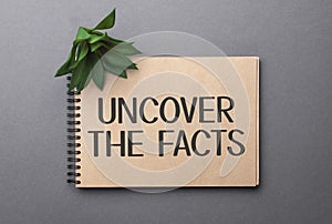 UNCOVER THE FACTS text on craft colored notepad and green plant on the dark background