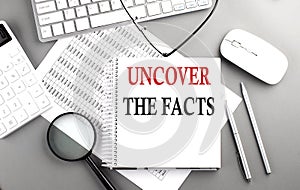 UNCOVER THE FACTS text on notepad on chart with keyboard and calculator on grey background