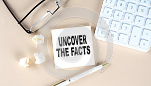 UNCOVER THE FACTS text on sticky with pen ,calculator and glasses on a beige background