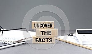 UNCOVER THE FACTS text on wooden block with notebook,chart and calculator, grey background