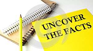 UNCOVER THE FACTS text written on a yellow paper with notebook