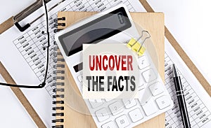 UNCOVER THE FACTS word on sticky with clipboard and notebook, business concept