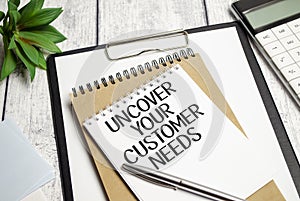 uncover your customer needs text on white notebook and pen on wooden background