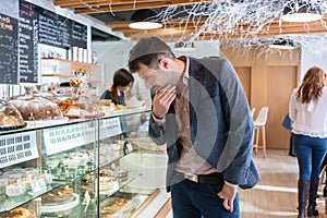 Undecided man looking at various cakes exposed in the showcase
