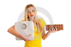 Undecided woman holding scale and chocolate uncertain wether to