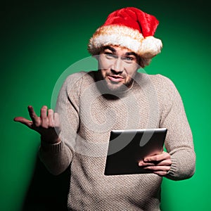 Undecided young santa man holding a tablet pad