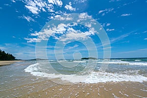 Under the blue sky and white clouds, the waves wash on the beach, and the small island in the distance