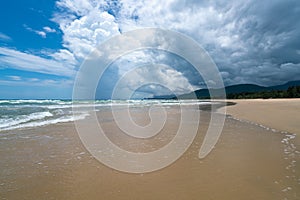 Under the blue sky and white clouds, the waves wash on the beach, and the small island in the distance