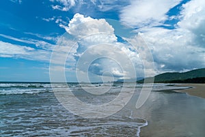 Under the blue sky and white clouds, the waves wash on the beach, and the small island in the distance