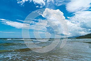 Under the blue sky and white clouds, the waves wash on the beach, and the small island in the distance