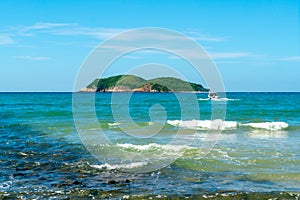 Under the blue sky and white clouds, the waves wash on the beach, and the small island in the distance