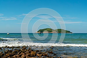 Under the blue sky and white clouds, the waves wash on the beach, and the small island in the distance