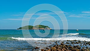 Under the blue sky and white clouds, the waves wash on the beach, and the small island in the distance