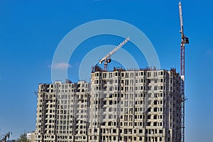 Under construction building against the sky and tower cranes. Unfinished construction house. Tower cranes against a blue sky. New