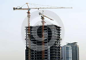 Under construction tall building skyscraper with yellow construction cranes next to it