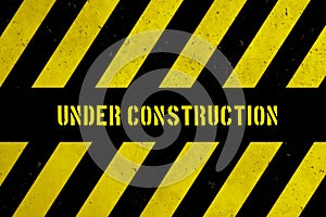 Under construction warning danger sign with yellow and black stripes painted over concrete wall coarse facade texture background.