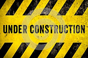 Under construction warning sign text with yellow black stripes painted over concrete wall cement facade texture background