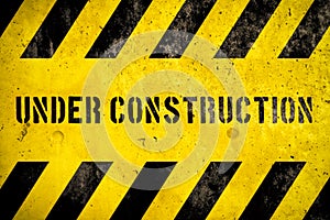 Under construction warning sign text with yellow black stripes painted over concrete wall coarse facade as texture background