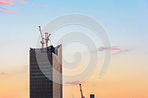 Under constuction skyscaper building with industrial cranes in sunset sky