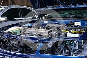 Under repair blue car with many unmounted parts on the engine bay with the hood opened at the auto garage